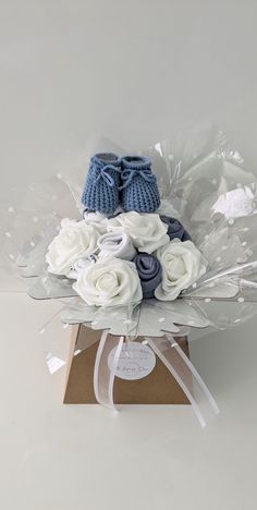 a bouquet of white and blue flowers with baby shoes on top in a cardboard box