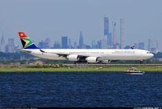 an airplane that is sitting in the grass near some water and a city skyline behind it