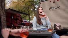 two women sitting at a table with wine glasses in front of them and a trailer behind them