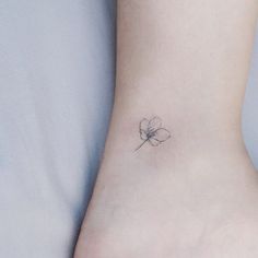 a small flower tattoo on the ankle is shown in black and white ink, with an outline of a single flower behind it