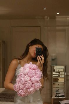 a woman taking a selfie in front of a mirror holding a bouquet of pink peonies