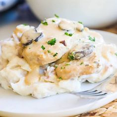 a white plate topped with mashed potatoes covered in gravy next to a fork