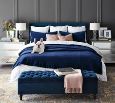 a blue bed with white sheets and pillows in a gray room next to two nightstands