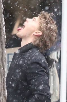 a young man standing next to a tree in the snow with his mouth open and tongue out