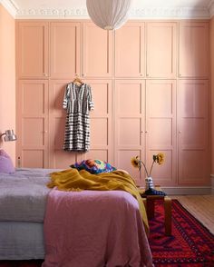 a bedroom with pink walls and bedding in the foreground is a white lamp