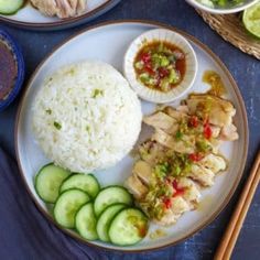 a plate with rice, cucumbers and chicken on it next to chopsticks