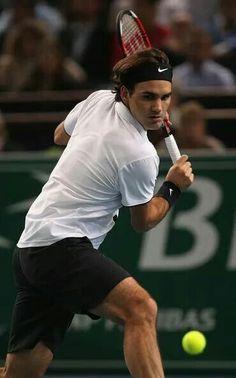 a man swinging a tennis racquet at a ball on a court with people in the background