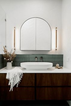 a white sink sitting on top of a wooden counter next to a mirror and vase with flowers