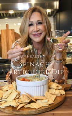 a woman sitting at a table with chips and wine in front of her, holding a spoon