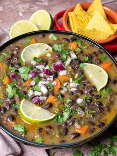 a bowl of black bean soup with tortilla chips and limes on the side