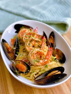 a white bowl filled with pasta and shrimp on top of a wooden table next to a blue towel