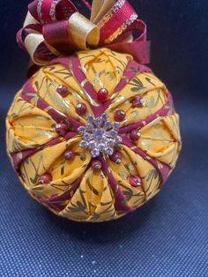 a yellow ornament with red and gold ribbons on it's top, sitting on a blue surface