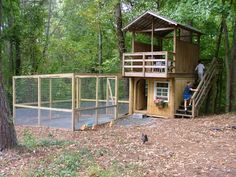 two people are standing on the porch of a small house in the woods with chicken cages around it