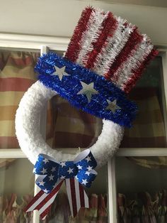 a patriotic wreath with stars and stripes on it hanging in front of a window decorated with red, white, and blue tinsel