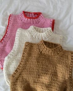 three knitted sweaters laying on top of a white bed next to each other