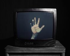 an old television with the hand on it's screen in front of a black background