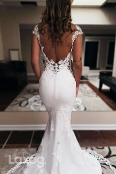 a woman in a white wedding dress looking at the back of her gown, standing on a rug