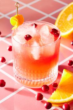 an orange and cranberry cocktail garnished with cherries on a pink table