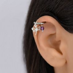 a woman's ear is adorned with two small silver dragonflys and amethyst stones