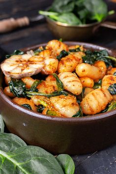 a bowl filled with shrimp and spinach on top of a table next to some greens