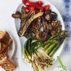 grilled vegetables on a white plate next to other foods and dipping sauce in a small bowl