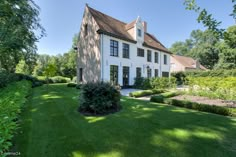 a large white house sitting in the middle of a lush green field with lots of trees