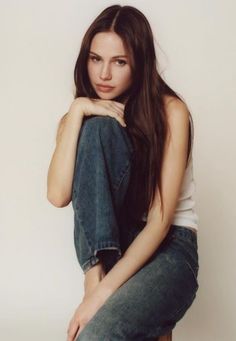 a young woman sitting on top of a wooden chair with her legs crossed and looking at the camera