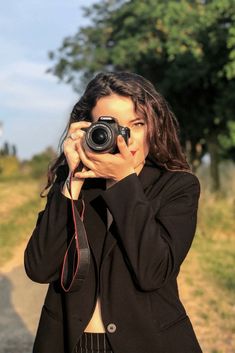 a woman taking a photo with her camera on the side of the road in front of some trees