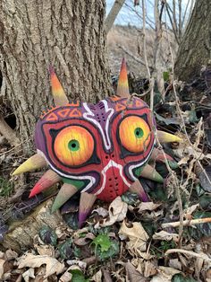 a colorful mask sitting next to a tree on the ground in front of some leaves