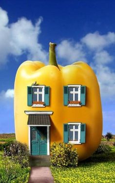 a house made out of a giant yellow pepper sitting on top of a lush green field