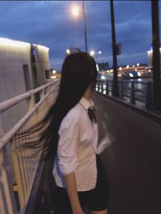 a woman with long hair standing on a bridge looking at the city lights in the distance