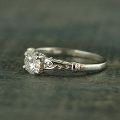 a white gold engagement ring with an old - fashioned style diamond in the center, sitting on a wooden surface