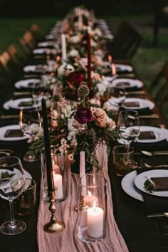 a long table is set with candles and plates for an elegant dinner party in the backyard