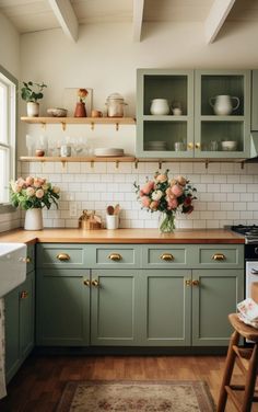 a kitchen with green cabinets and flowers in vases