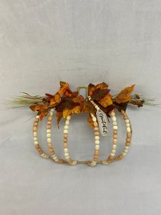 three white and brown beaded pumpkins with autumn leaves on them, hanging from a wall