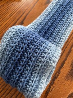 a blue and gray knitted hat sitting on top of a wooden table next to a cup