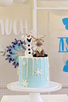 a frosted cake decorated with snowmen and reindeer figurines sitting on top of it