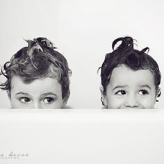 two young children with curly hair are looking over a white surface and one is staring at the camera