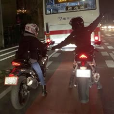 two motorcyclists are riding down the street with their arms in the air