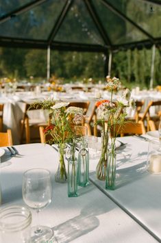 several vases filled with flowers sitting on top of a white tablecloth covered table