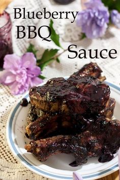 two pieces of ribs covered in blueberry sauce on a plate next to purple flowers