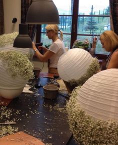 three women working on paper lanterns in a living room with flowers and greenery around them