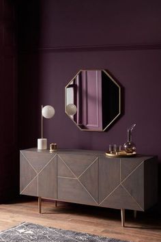 a room with purple walls and a gold mirror on the sideboard in front of it