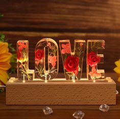 the letters love are made out of glass and decorated with red roses, surrounded by yellow sunflowers