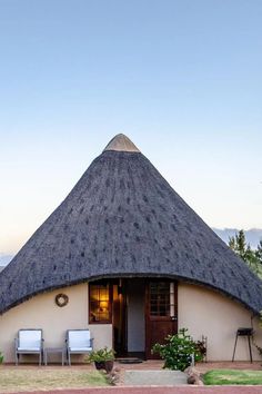 a thatched roof house with two chairs in front