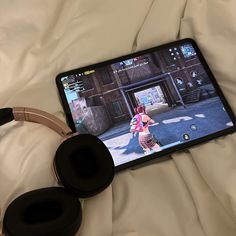 a tablet with headphones on top of it sitting on a white bed next to a pair of headphones