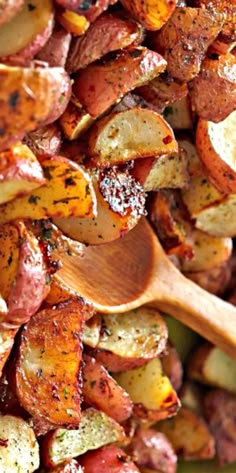 a close up of a wooden spoon in a bowl of potatoes with seasoning on top