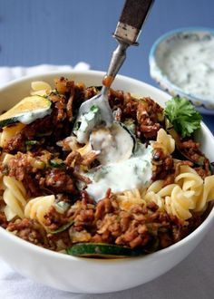 a white bowl filled with pasta and meat next to a small bowl of sour cream