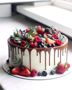 a cake with berries and chocolate drizzled on top is sitting on a window sill