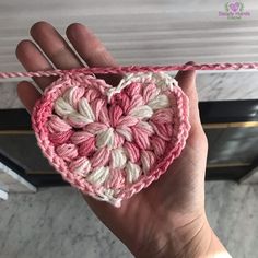 someone is holding up a crocheted heart